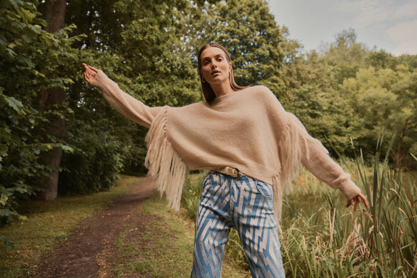 Michonet – Pull Flecos Beige, mannequin femme portant un pull beige à franges et un pantalon à motifs bleus