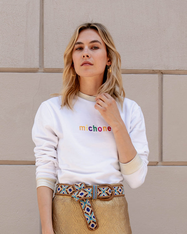 Michonet – Sweat Logo White, mannequin blonde portant un sweat blanc et une jupe dorée avec une ceinture