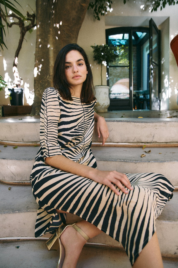 Michonet – Robe Hoja Beig, mannequin assise de face, robe zébrée beige et noire, chaussures dorées