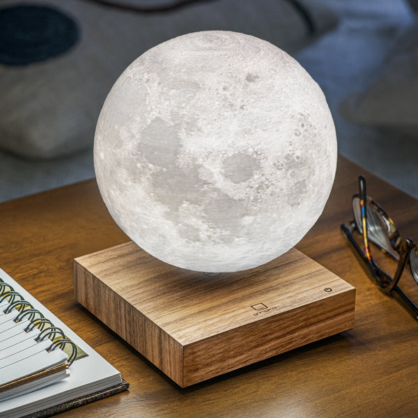Gingko Design – Lampe Smart Moon - Natürlicher Walnussbaum, schwebende Mondlampe auf Holzsockel, auf einem Tisch stehend