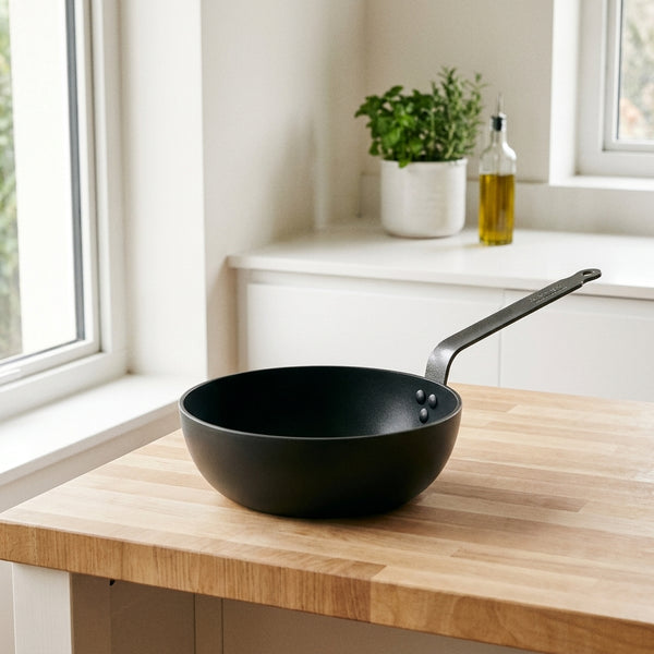 De Buyer – Choc Intense - Sauteuse Antiadhésive - Aluminium Forgé - Noir, une poêle noire en fonte posée sur un plan de travail en bois
